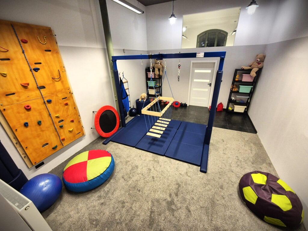 Sala do terapii integracji sensorycznej w gabinecie Siódmy Zmysł w Olsztynie z podwiesiem, ścianką wspinaczkową, pufami i sprzętem SI.